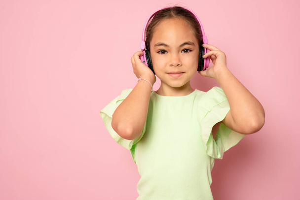 Beautiful cute happy little girl with headphones standing isolated over pink background. - Foto, Imagem