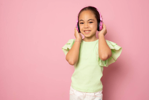 Schöne niedliche glückliche kleine Mädchen mit Kopfhörern stehen isoliert über rosa Hintergrund. - Foto, Bild