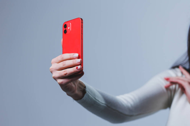 El nuevo teléfono inteligente rojo en manos femeninas. Mujer escribiendo un mensaje en el teléfono en primer plano - Foto, Imagen