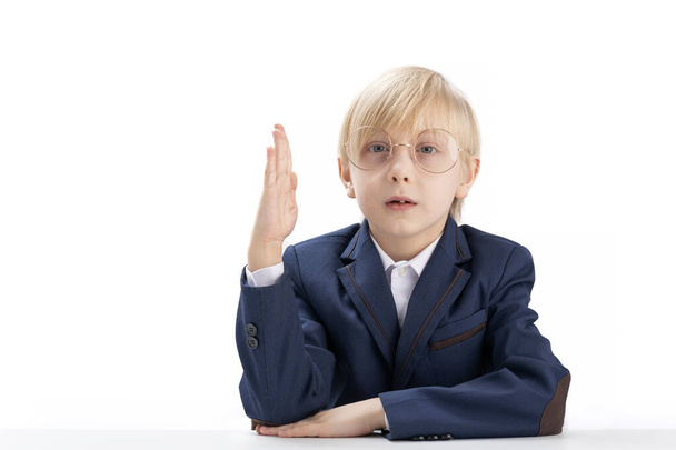 Primary school student sits at table or desk with hand raised. Portrait of straight-A student boy is isolated on white background - Foto, immagini