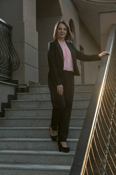 Successful woman in business clothing ot the stairs. Woman wearing black suit. Young business woman. - 写真・画像