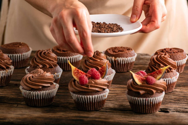 Pastelaria chef polvilha com cupcakes de chocolate com framboesas e figos. Close up de preparação de muffin - Foto, Imagem