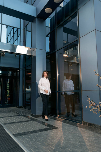 Full-length portrait of young business woman in formal attire against the backdrop of modern building with glass facade - Valokuva, kuva