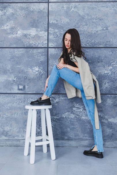 Beautiful woman with slender legs in jeans and fashionable outerwear with a raincoat, stylish leather shoes. Women's image in spring style - Foto, afbeelding