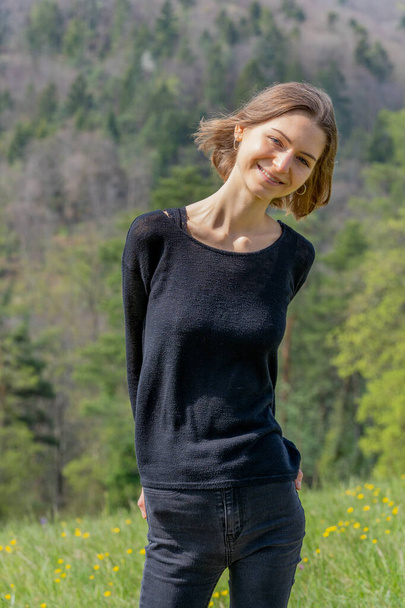 Πορτρέτο της νεαρής όμορφης γυναίκας που φοράει μαύρα ρούχα χαμογελώντας στην κάμερα στη φύση της Ελβετίας την άνοιξη. - Φωτογραφία, εικόνα