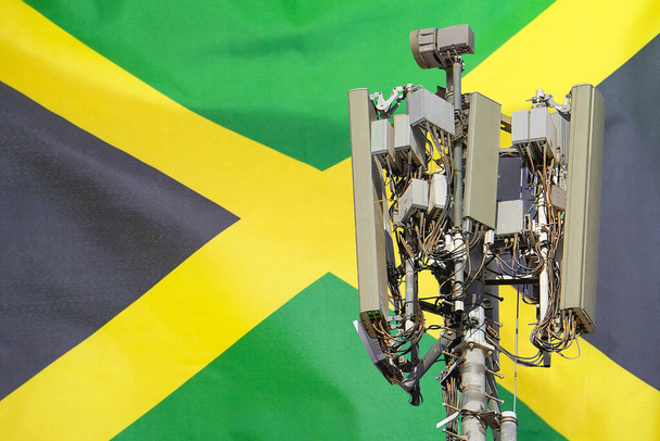 Torre de telecomunicaciones con una antena de red celular 5G contra bandera de Jamaica. Torre de telecomunicaciones de comunicación celular 5G. Uso de tecnología 5G en torres de telecomunicaciones en Jamaica - Foto, Imagen