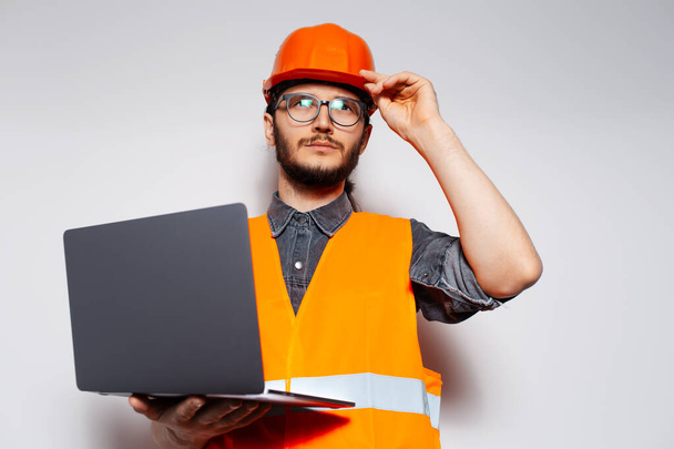 Молодий інженер, який використовує ноутбук на білому, носить помаранчеве будівельне обладнання
. - Фото, зображення