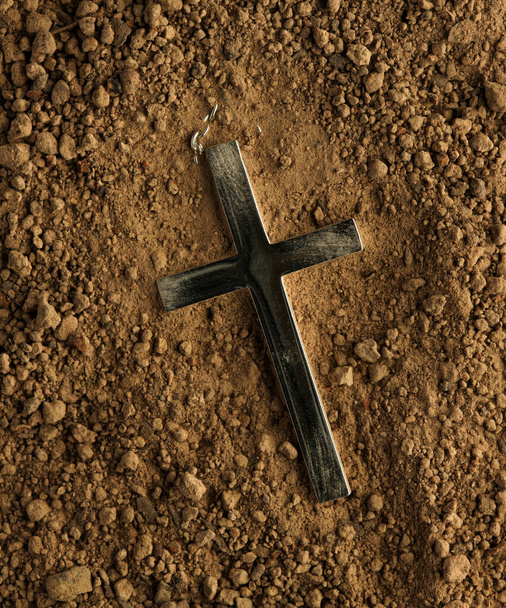 Christian cross necklace buried in ground with the dirt brushed away from the crucifix. - Фото, зображення