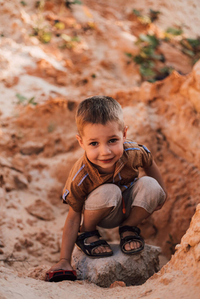 Ένα μικρό αγόρι κάθεται στην άμμο παίζοντας με ένα μικρό αυτοκίνητο - Φωτογραφία, εικόνα