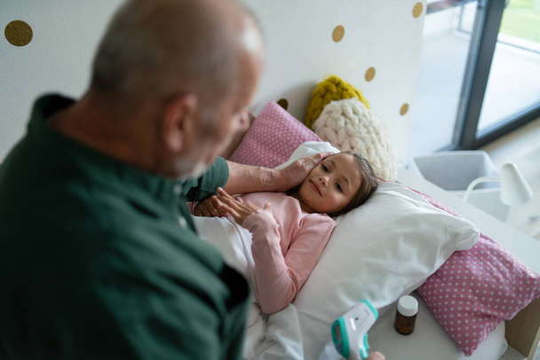 Grandfather taking care of his ill granddaughter lying in bed. - Valokuva, kuva