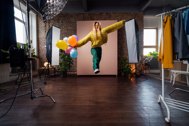 Fashion studio portrait of a happy young woman with balloons jumping, backstage of photoshooting . - Фото, зображення