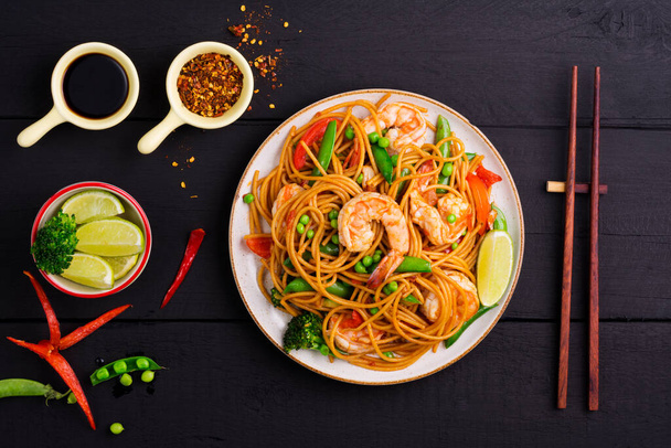 Smažené špagety nebo smažené nudle se zeleninou a krevetami na talíři. na tmavém černém pozadí, horní pohled - Fotografie, Obrázek