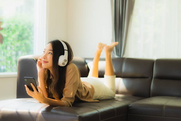 Portrait beautiful young asian woman use smartphone or cellphone on sofa with headphone for listen music - Фото, изображение