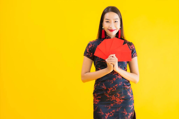 肖像美しい若いアジアの女性は、黄色の隔離された背景に中国の旧正月の概念のための現金と中国のドレスを着ている - 写真・画像