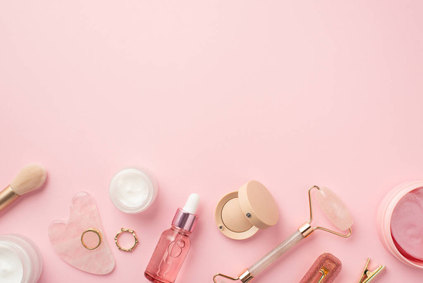 Top view photo of makeup brush rose quartz roller gua sha pink eye patches glass bottles eyeshadow hairpins and gold rings on isolated pastel pink background with copyspace - 写真・画像