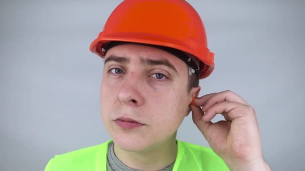 Dělník v tvrdém klobouku a zelené vestě si nasadí špunty do uší. Průmyslová bezpečnost. Ochrana proti hluku v průmyslu. Dodržování pravidel chování při hlasité práci. Pomerančové ucpávky - Záběry, video