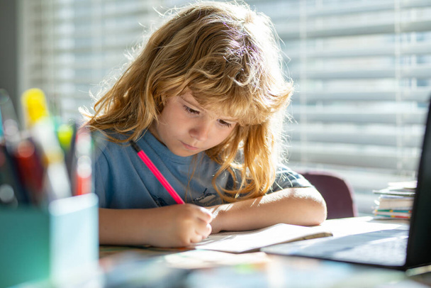 Child writing at school. Portrait of school kid boy siting on table doing homework. Child holding pencil and writing. Boy drawing on white paper at the table. - Foto, afbeelding