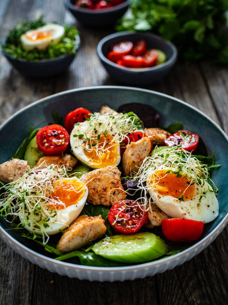 Chicken salad - chicken nuggets, hard boiled eggs, cherry tomatoes, lettuce, cucumber and sprouts on wooden table  - Фото, зображення