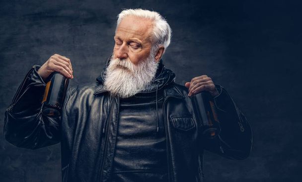 Elderly man biker holding two bottles against dark background - Foto, Bild