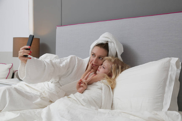 Madre y su niña mirando el teléfono celular en la cama - Foto, Imagen