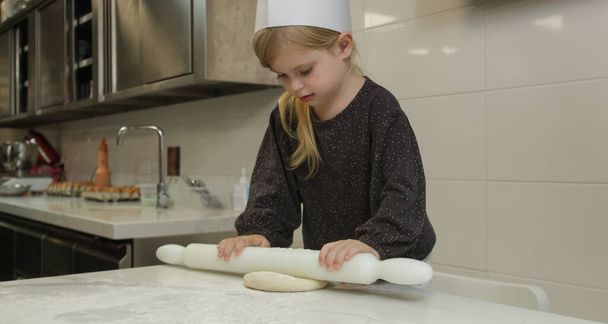 Kislány, aki főzőtanfolyamon tanul tésztát keresni. Süteményosztály gyerekekkel kis séf. - Fotó, kép