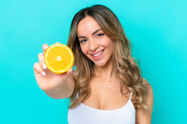 Young caucasian woman isolated on blue background holding an orange - Foto, afbeelding