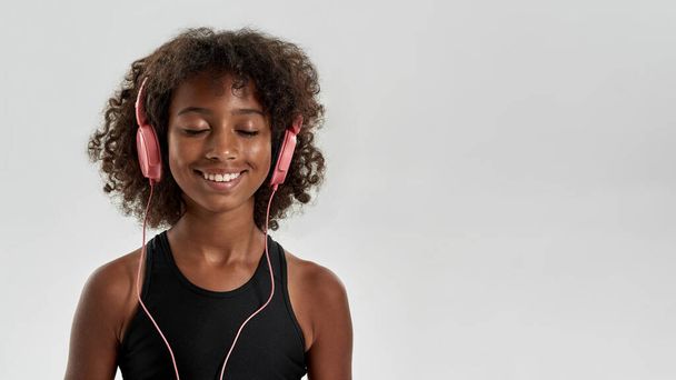 Pleased black girl listening music in earphones - Foto, Imagen