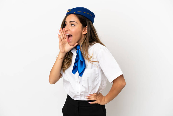 Airplane stewardess over isolated white background shouting with mouth wide open to the lateral - Foto, afbeelding