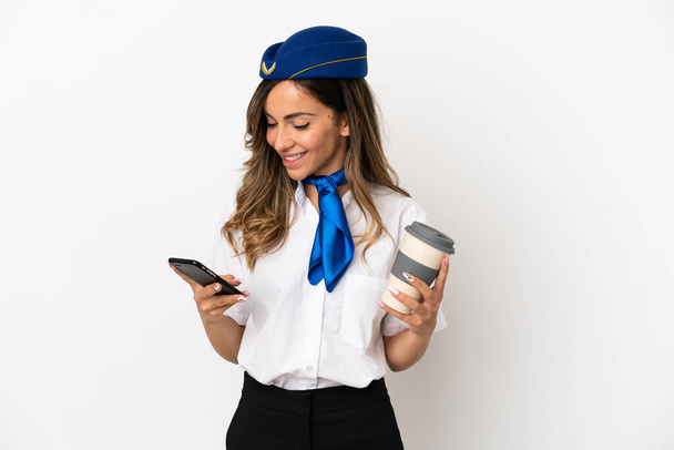 Stewardessa samolotu nad odizolowanym białym tle trzymając kawę do zabrania i mobilny - Zdjęcie, obraz
