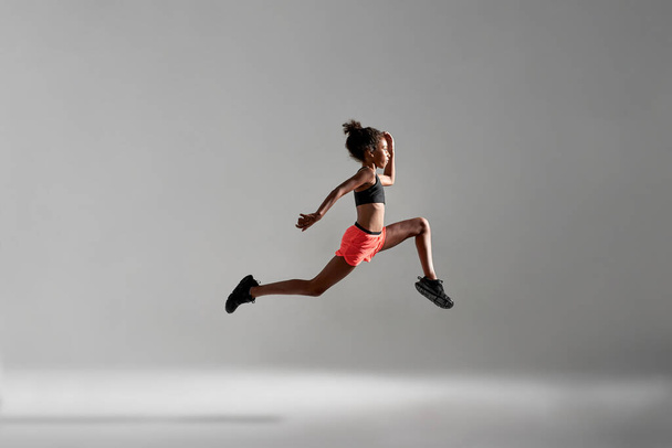 Side view of athletic black girl jump during run - Fotó, kép