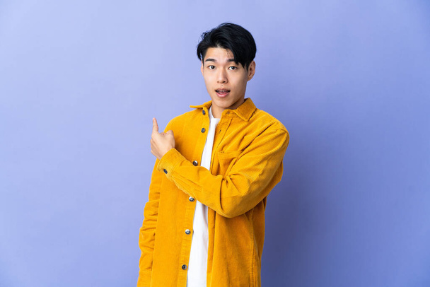 Young Chinese man isolated on purple background surprised and pointing side - Foto, Bild