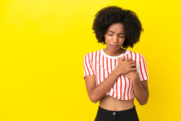 Joven mujer afroamericana aislada sobre fondo amarillo con dolor en el corazón - Foto, imagen