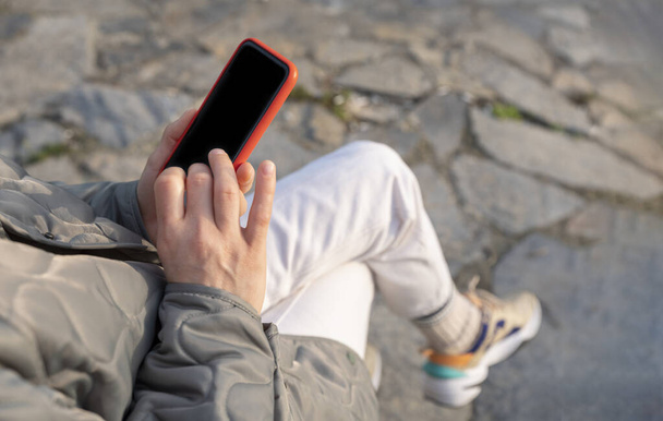 жінка використовує мобільний телефон, сидячи на лавці в парку
 - Фото, зображення