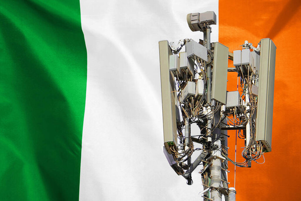 Telecommunications tower with a 5G cellular network antenna agains flag of Ireland. Telecommunication tower of 5G cellular communication. 5G technology usage on telecommunications towers in Ireland - Photo, Image