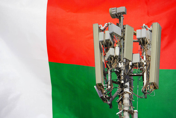 Telecommunications tower with a 5G cellular network antenna agains flag of Madagascar. Telecommunication tower of 5G cellular communication. 5G technology usage telecommunications towers in Madagascar - Foto, Imagem