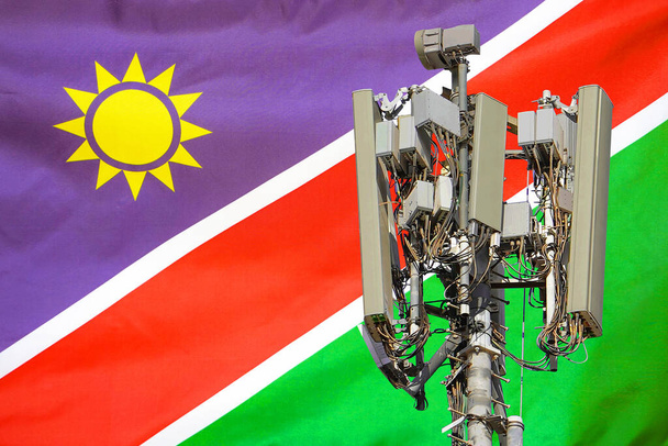 Telekommunikationsturm mit einer 5G-Mobilfunkantenne gegen die Flagge Namibias. Telekommunikationsturm für 5G-Mobilfunk. Nutzung der 5G-Technologie auf Telekommunikationstürmen in Namibia - Foto, Bild