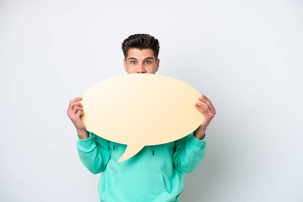 Young handsome caucasian man isolated on white bakcground holding an empty speech bubble hiding behind it hiding behind it - Photo, image
