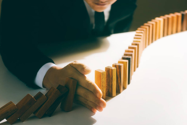 Risk management, business man hand Stop the continuous falling of wooden dominoes, stop the impact of the business crisis. hedging Solving business problems for success. - Foto, imagen
