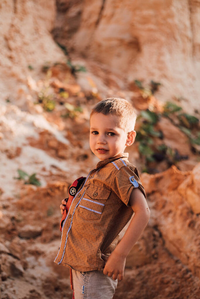 Маленький мальчик стоит посреди песка и держит в руках игрушку. - Фото, изображение