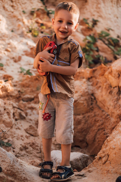 Ein kleiner Junge steht mitten im Sand und hält ein Spielzeug in den Händen - Foto, Bild