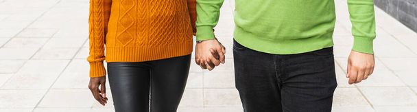 Close-up view of an interracial couple holding hands while walking together outdoors on the street. - 写真・画像