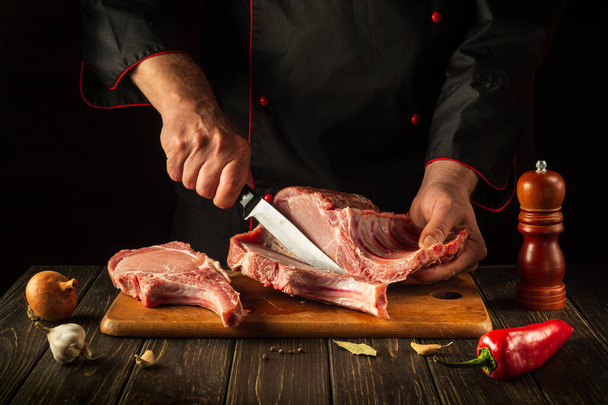 The cook cuts raw ribs on a cutting board before barbecuing. European cuisine. Cooking delicious food in the hotel kitchen. - Фото, зображення