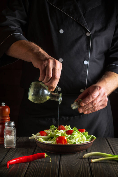 Ammattikokki kaataa oliiviöljyä salaattikulhoon. Ruoanlaitto maukasta ja terveellistä ruokaa joukko vitamiineja. Resepti hotellille - Valokuva, kuva