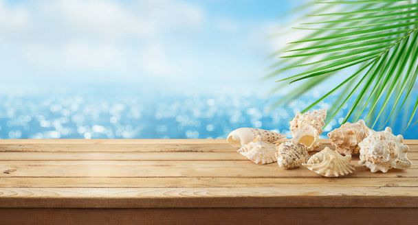 Порожній дерев'яний стіл з черепашками на фоні морського пляжу. Літній макет для дизайну та відображення продуктів
. - Фото, зображення