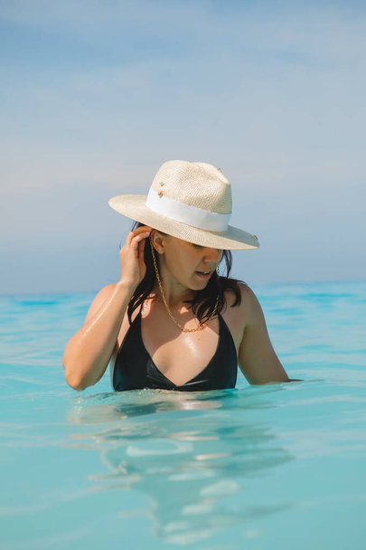 γυναίκα με λευκό καπέλο και μαύρο μαγιό σε μπλε νερά καλοκαιρινές διακοπές - Φωτογραφία, εικόνα