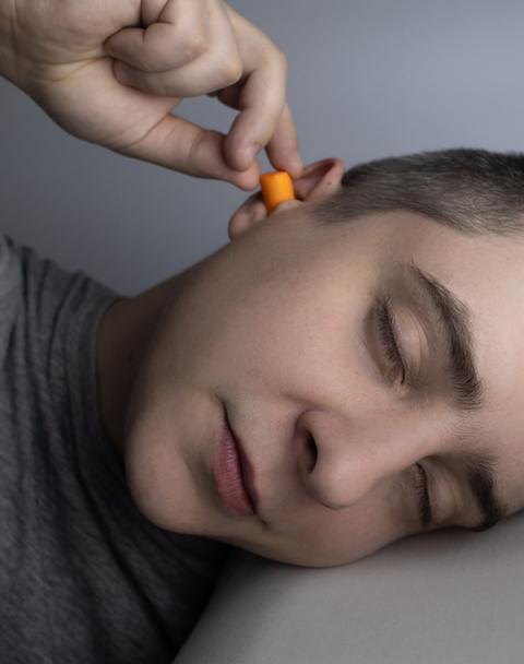 Mies laittaa korvatulpat. Oranssin äänivallin lähikuva. Nuku hyvin. ENT lääkäri neuvoo oranssi kuulokkeet vähentää ympäristön melua. Lisääntynyt herkkyys äänille. - Valokuva, kuva