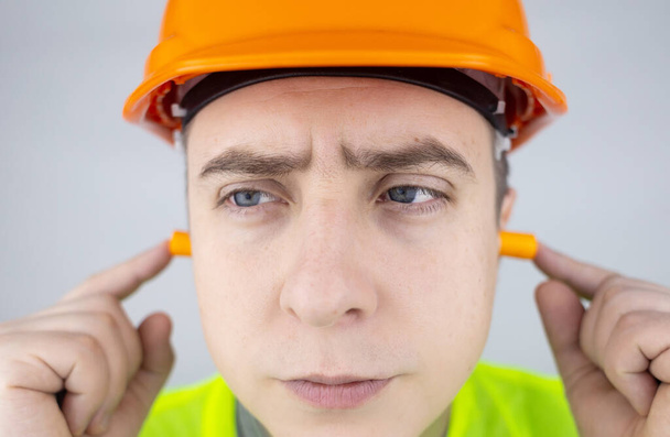 A worker in a hard hat and green vest puts on ear plugs. Industrial safety. Industrial noise protection. Compliance with the rules of conduct at loud work. Orange ear plugs - Foto, imagen