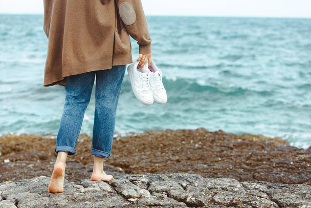 žena kráčí bosá u moře a drží se za ruce bílé boty. letní prázdniny. příroda unie - Fotografie, Obrázek