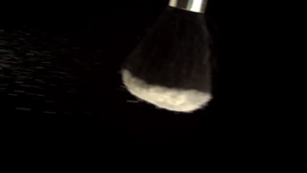 Polvo cosmético para la cara se vierte de un cepillo sobre un fondo negro - Metraje, vídeo
