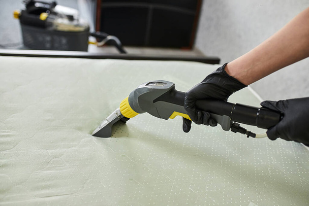 Cleaning service company employee removing dirt from furniture in flat with professional equipment. Female housekeeper arm cleaning the mattress on the bed with washing vacuum cleaner close up - 写真・画像